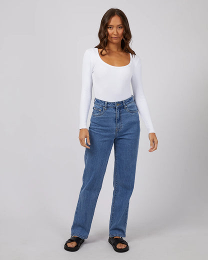 Woman wearing a white long-sleeve top and blue jeans on a gray background