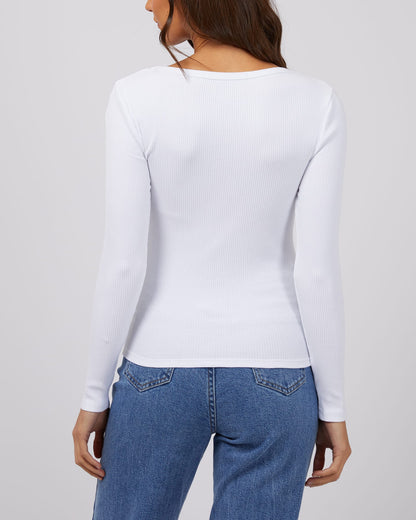 Person wearing a white long-sleeve top and blue jeans on a plain background