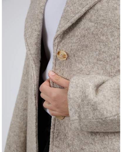 Close-up of a person wearing a beige coat with a button, on a light gray background