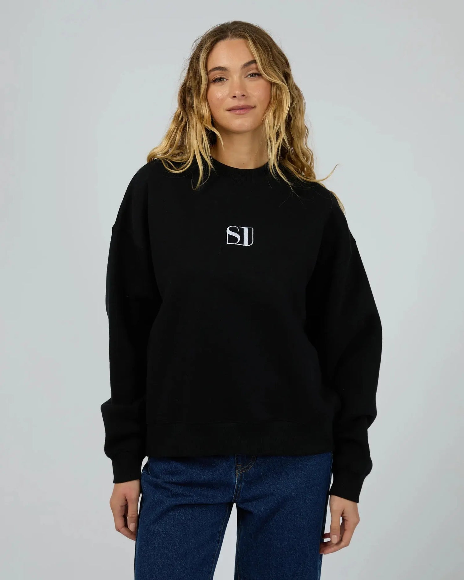 Person wearing a black sweatshirt with a logo on a plain background