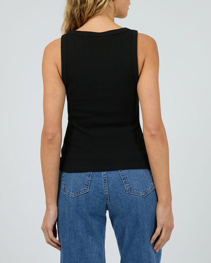 Person wearing a black sleeveless top and blue jeans on a plain background