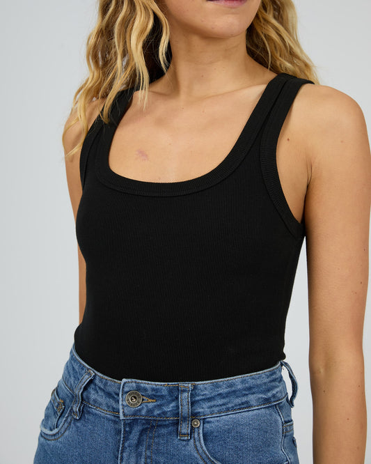 Person wearing a black tank top and blue jeans against a plain background