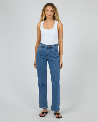 Woman wearing blue jeans and a white tank top on a plain background