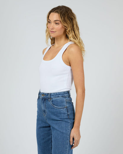 Woman wearing a white tank top and blue jeans on a plain background