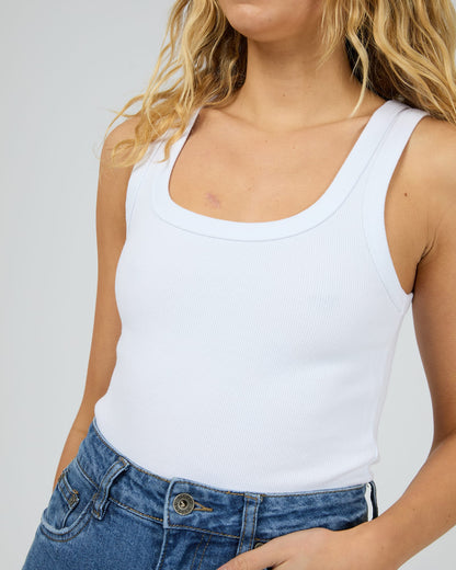 Person wearing a white tank top and blue jeans against a plain background