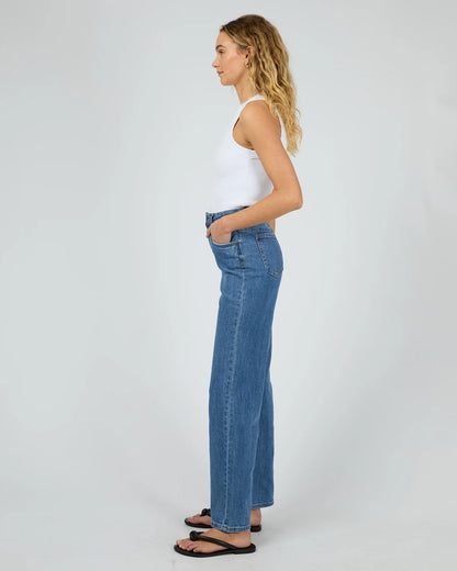 Woman wearing blue jeans and a white tank top on a plain background