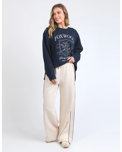 Woman wearing a navy sweatshirt with 'Foxwood' branding and cream pants on a white background