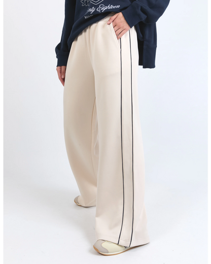 Beige wide-leg pants with a black stripe worn by a person on a white background