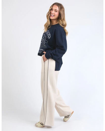 Woman wearing a navy sweater and white pants with a side stripe on a white background