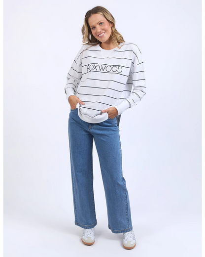 Woman wearing a striped sweater with 'Foxwood' branding and blue jeans on a white background
