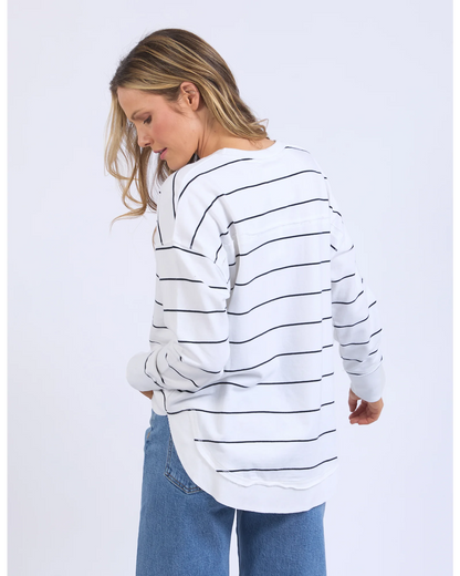 Woman wearing a white and black striped sweater with blue jeans on a light gray background
