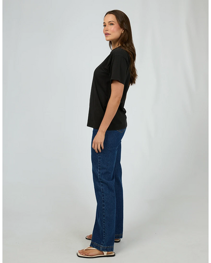 Woman wearing a black t-shirt and blue jeans standing against a white background