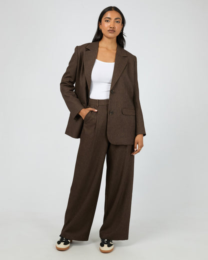 Woman wearing a brown suit with a white top on a plain background