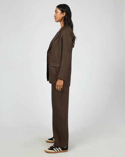 Person wearing a brown suit with black Adidas shoes on a white background