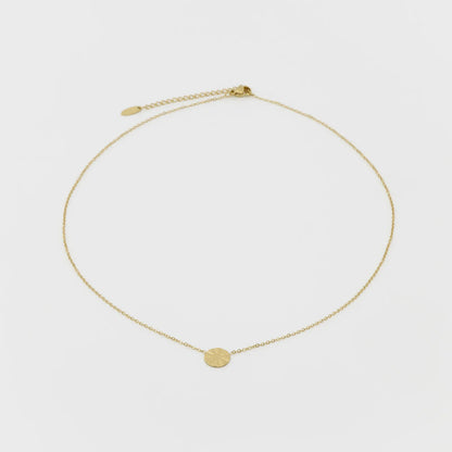 Gold necklace with a small round pendant on a light gray background