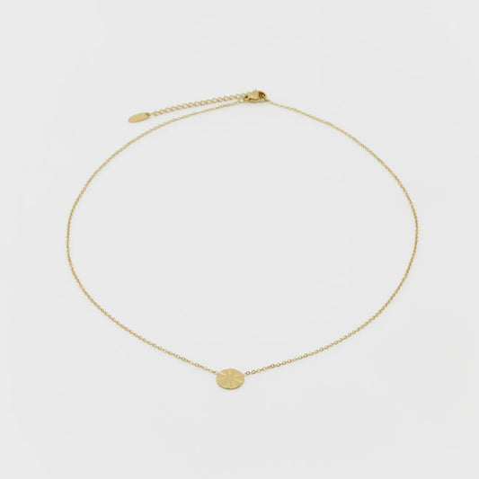 Gold necklace with a small round pendant on a light gray background