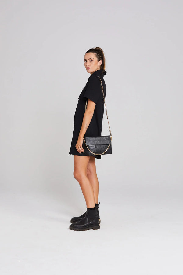 Woman wearing a black dress and black boots with a black handbag on a white background