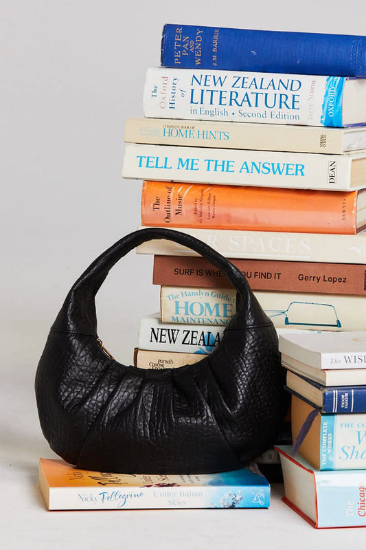 Black leather handbag on a stack of books with visible titles.