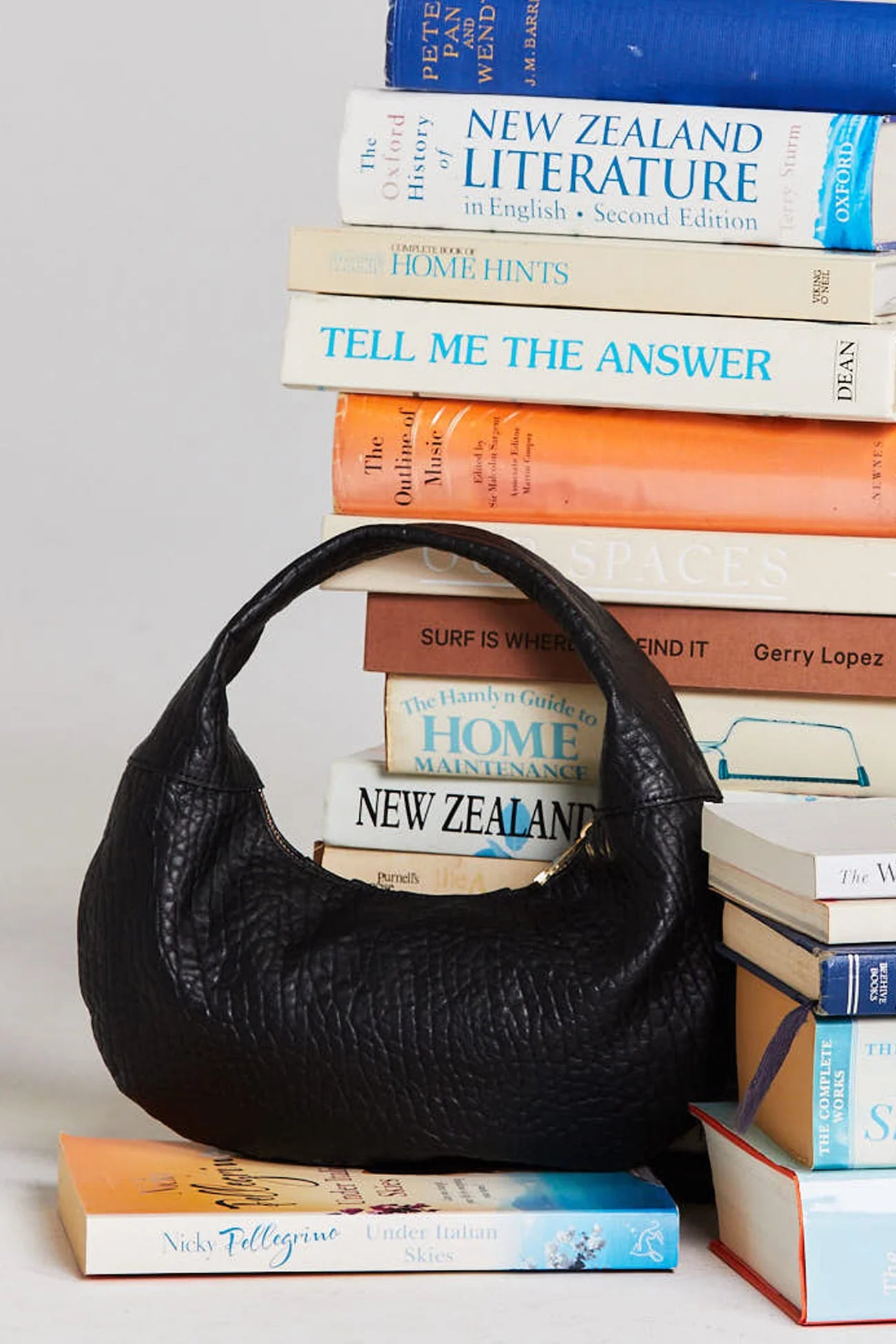Black handbag on a stack of books with visible book spines.