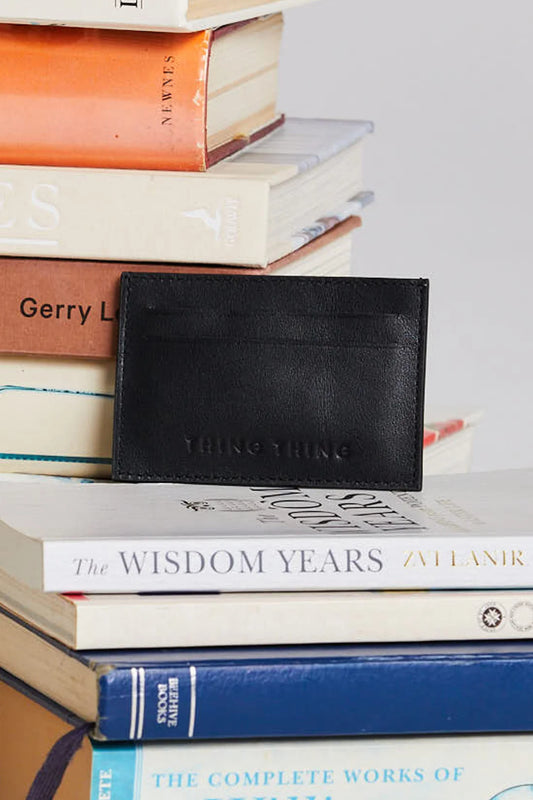 Black leather cardholder on a stack of books with visible titles.