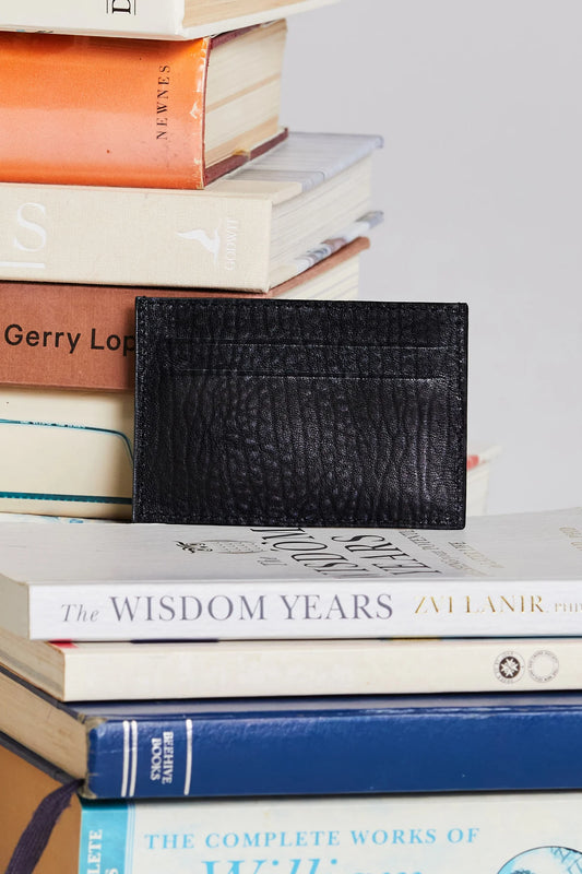 Black textured cardholder on a stack of books with visible titles.