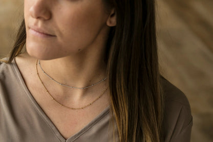 Model wearing layered bobble chain necklaces — close-up neck and décolletage shot
