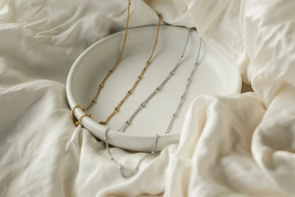 Silver and gold bobble chain necklaces on ceramic dish — flat lay product shot on white linen