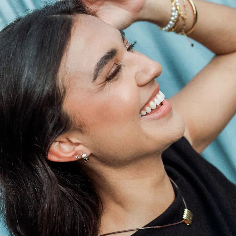 Woman with dark hair and earrings smiling against a light blue background