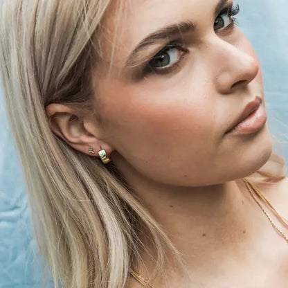 Close-up of a woman wearing gold earrings and a necklace against a light blue background