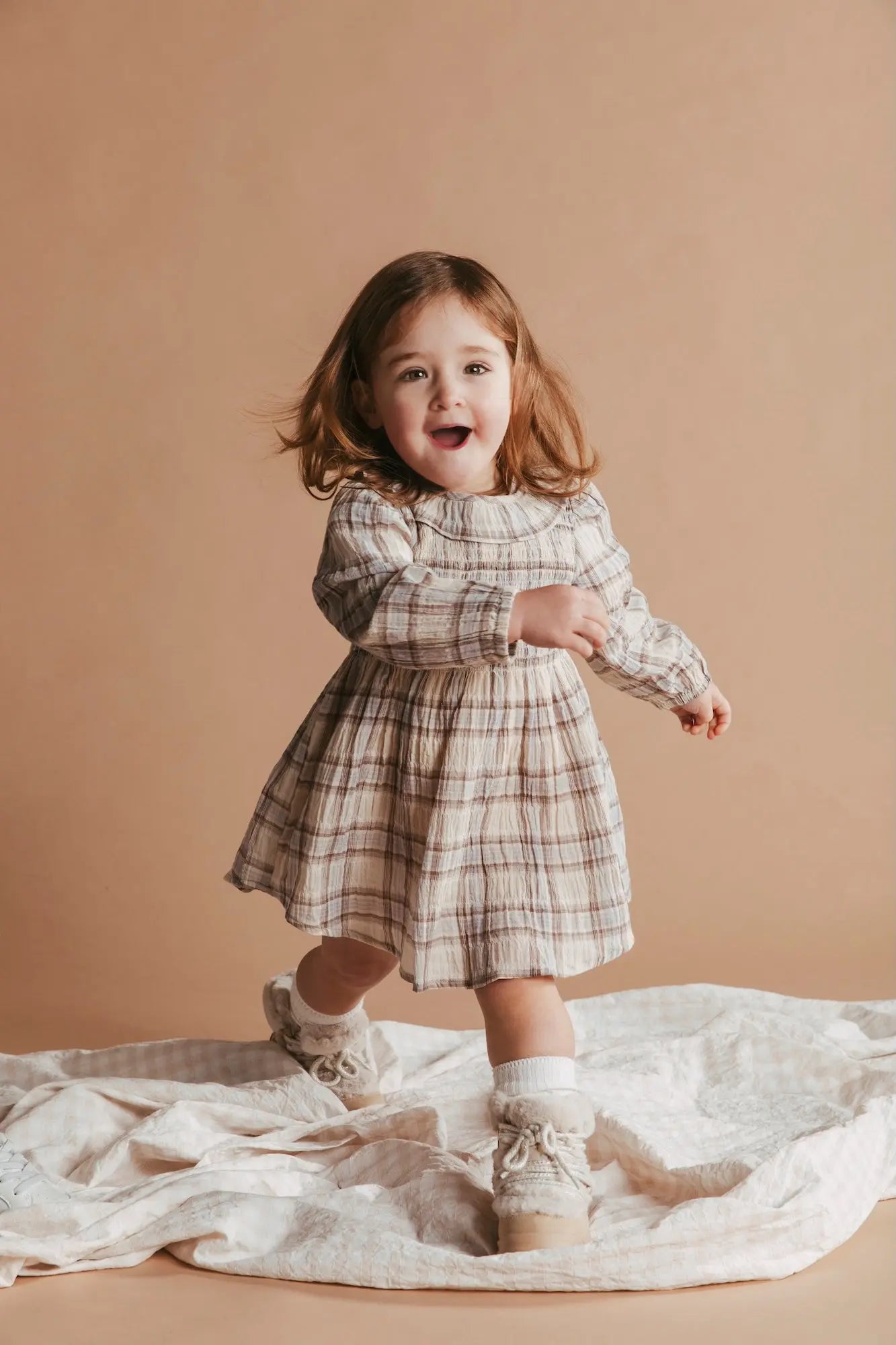 Child in a plaid dress standing on a beige background