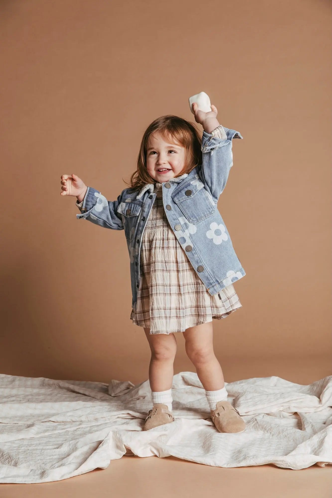 Child wearing a denim jacket and plaid dress on a beige background