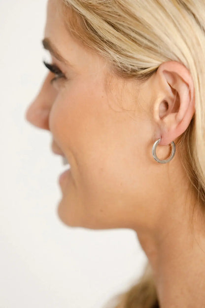 Close-up of a person wearing a silver hoop earring on a plain background