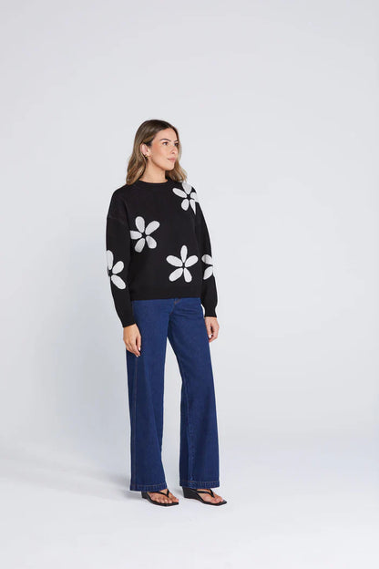 Woman wearing a black sweater with white floral patterns and blue pants on a white background