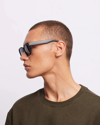 Person wearing sunglasses and a green sweater against a light gray background