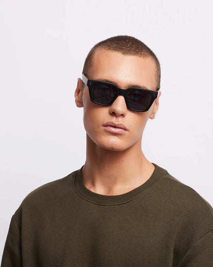 Person wearing dark sunglasses and a green sweater on a light gray background