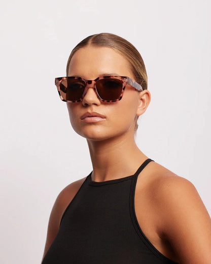 Woman wearing a black outfit and sunglasses on a light gray background