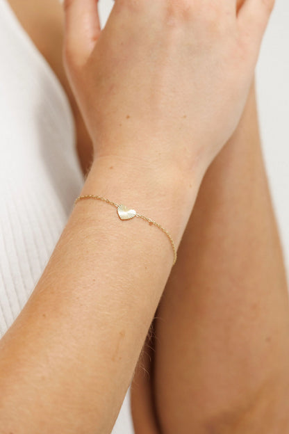 Gold heart-shaped bracelet on a wrist with a blurred background