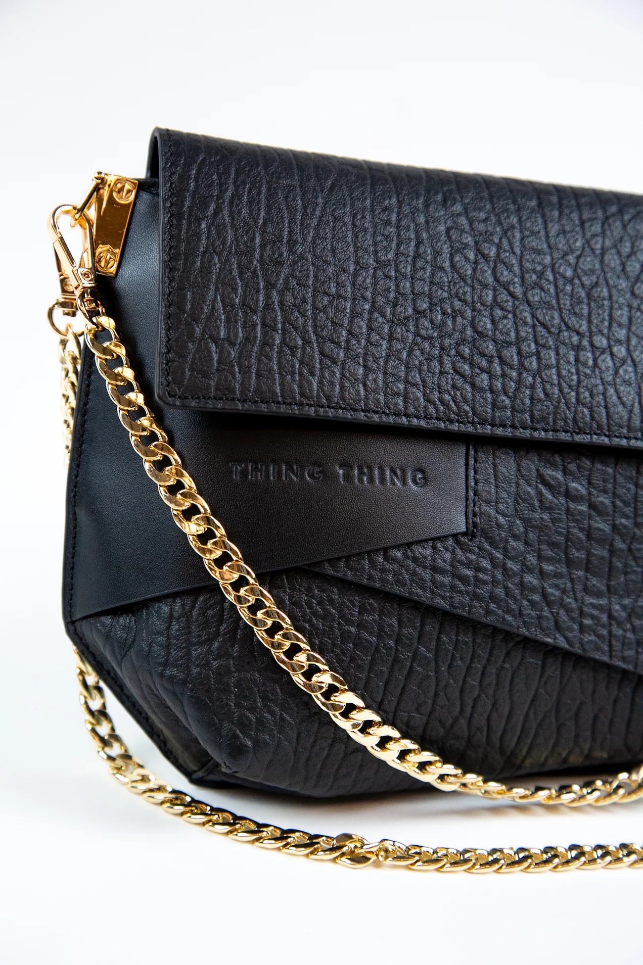Black textured handbag with a gold chain on a white background