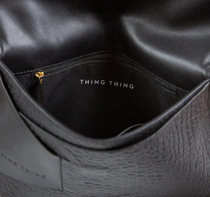 Close-up of a black leather bag with 'THING' branding.