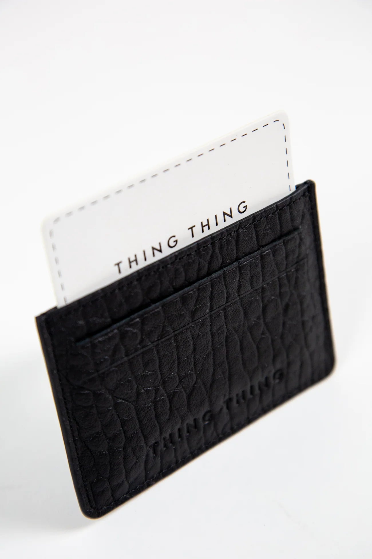 Black textured cardholder with a white card featuring 'THING THING' branding on a light gray background.
