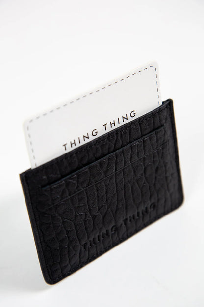 Black textured cardholder with a white card featuring 'THING THING' branding on a light gray background.
