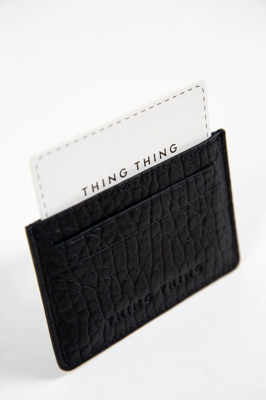Black textured cardholder with a white card featuring 'THING THING' branding on a light gray background.