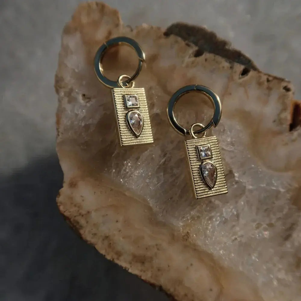 Gold earrings with heart-shaped gemstones on a textured stone surface