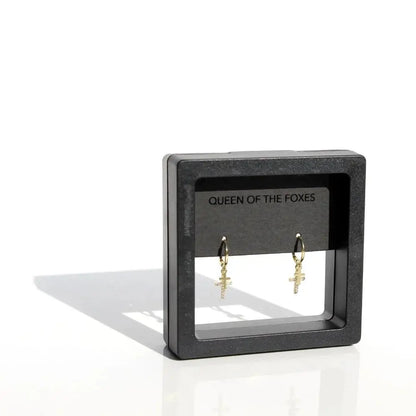 Gold earrings on a 'Queen of the Foxes' branded stand against a white background