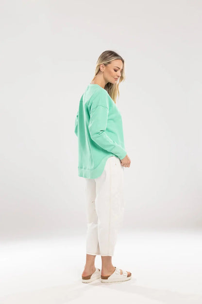 Woman wearing a light green sweater and white pants on a white background.Ena Sweat Green - The Rose Edit