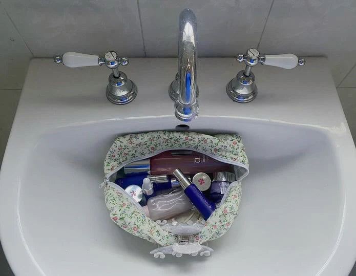Floral-patterned bag filled with toiletries on a white sink. Buttermilk Grace Carry All Bag Secret Garden - The Rose Edit