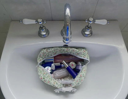 Floral-patterned bag filled with toiletries on a white sink. Buttermilk Grace Carry All Bag Secret Garden - The Rose Edit