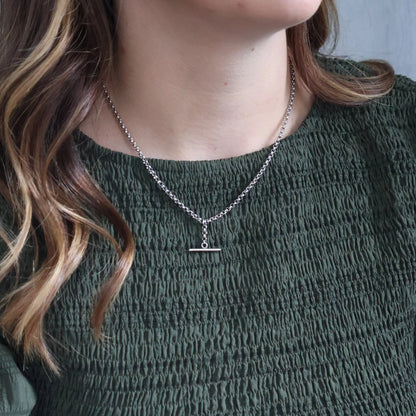 Person wearing a silver necklace with a small pendant against a neutral background. Large T Bar Necklace KatyB Jewellery