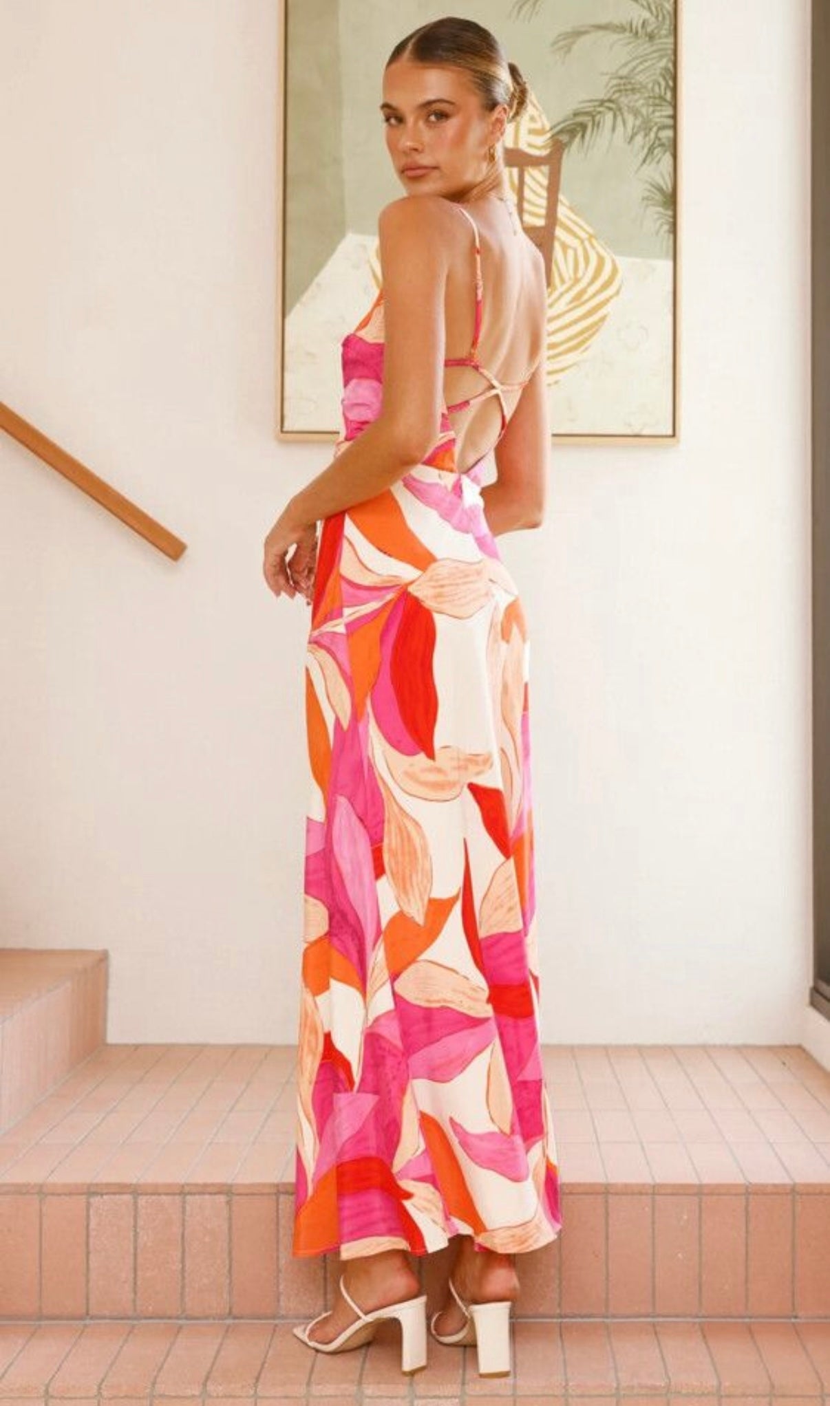 Woman in a colorful patterned dress standing indoors with a painting in the background