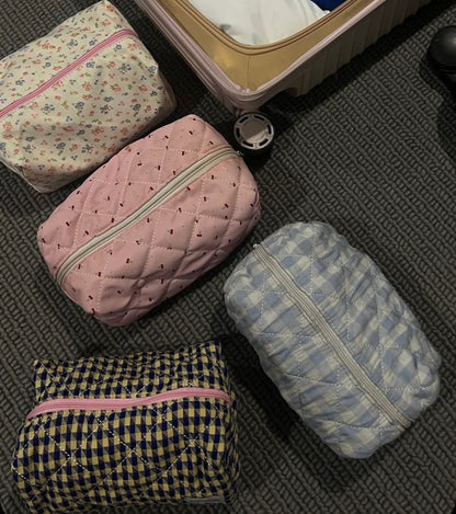 Four patterned packing cubes on a textured surface next to an open suitcase. Buttermilk Grace Carry All Bag Forget-Me-Not - The Rose Edit